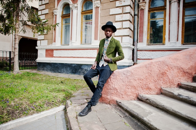 Mode portrait d'homme afro-américain noir sur la veste de velours vert et un chapeau noir s'asseoir sur le vieux manoir de fond d'escaliers