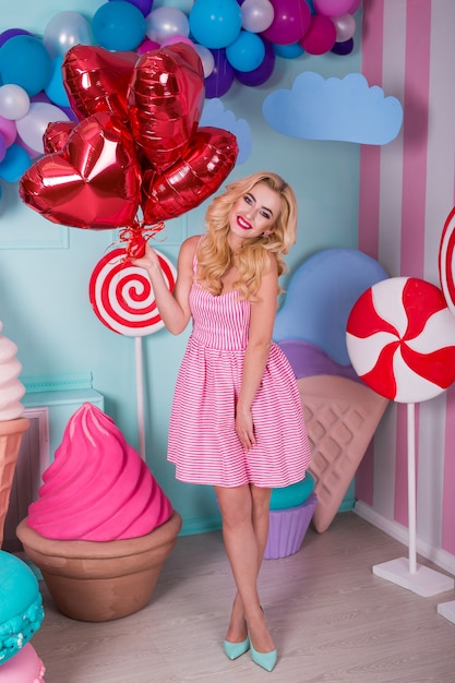 Mode portrait de jeune femme en robe rose avec des ballons à air, des bonbons sur un fond coloré.