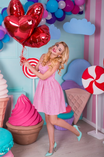 Mode portrait de jeune femme en robe rose avec des ballons à air chaud, des bonbons sur un coloré