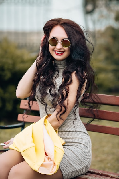 Mode portrait de jolie belle femme, longs cheveux bouclés, posant sur un banc de parc