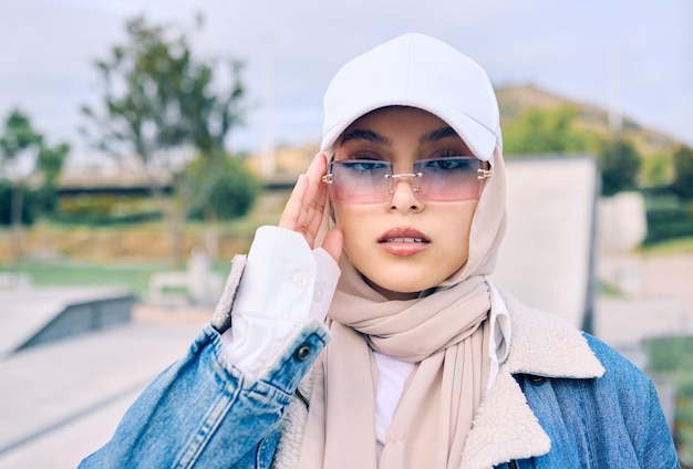 Mode portrait ou lunettes de soleil avec une femme islamique en plein air dans une casquette et une écharpe pour la foi musulmane de style contemporain ou le hijab avec une jeune femme arabe à la mode posant à l'extérieur dans des lunettes modernes