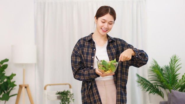 Mode de vie dans le concept de salon Jeune femme asiatique debout pour mélanger une salade de légumes dans un bol