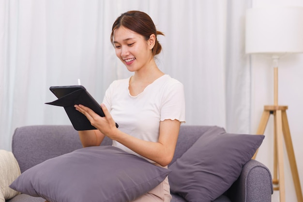 Mode de vie dans le concept de salon Jeune femme asiatique écrivant des données sur une tablette assise sur un canapé