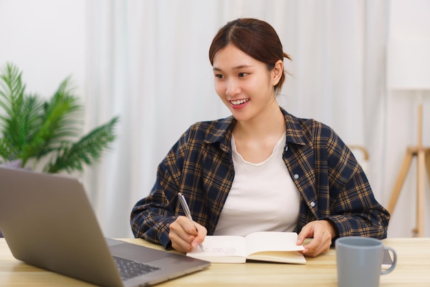 Mode de vie dans le concept de salon Jeune femme asiatique utilisant un ordinateur portable et prenant des notes sur un ordinateur portable