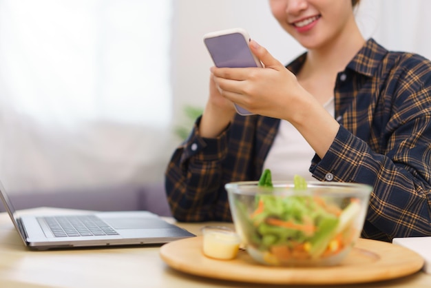 Mode de vie dans le concept de salon Jeune femme asiatique utilisant un smartphone et mangeant une salade de légumes