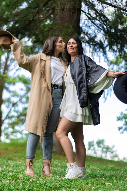 Mode de vie de deux filles avec des chapeaux s'embrassant sur la joue dans l'herbe Deux heureux meilleurs amis en chapeaux s'embrassant les joues à l'extérieur