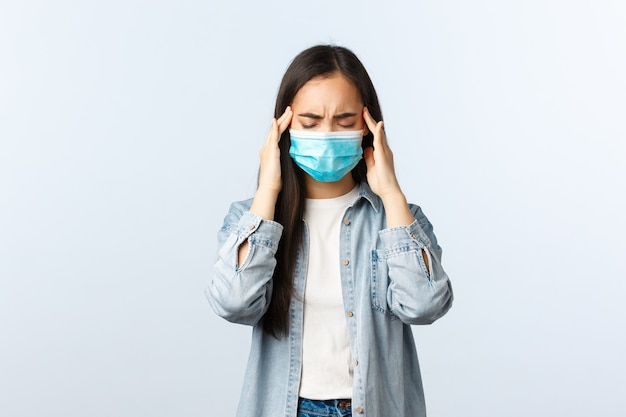 Mode de vie à distance sociale, vie quotidienne pandémique covid-19 et concept de loisirs. Une fille asiatique troublée a obtenu un test de coronavirus positif, se sentant malade, porte un masque médical, a des maux de tête ou des migraines.