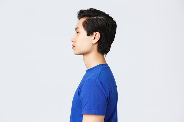 Mode de vie, émotions des gens et concept de beauté. Portrait de profil d'un hipster asiatique élégant et beau, d'un mec étrange avec une boucle d'oreille, d'une nouvelle coupe de cheveux du salon de coiffure, d'une expression normale à gauche