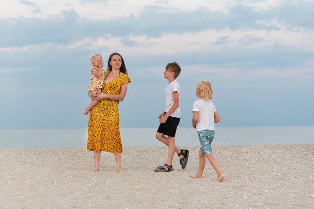 Mode de vie familial. Maman et trois enfants marchent le long de la plage de sable sur fond de mer.