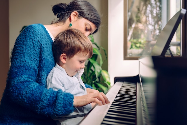 Mode de vie familial passer du temps ensemble à l'intérieur. Enfants avec vertu musicale et curiosité artistique. Maman enseigne à son fils à la maison des leçons de piano.