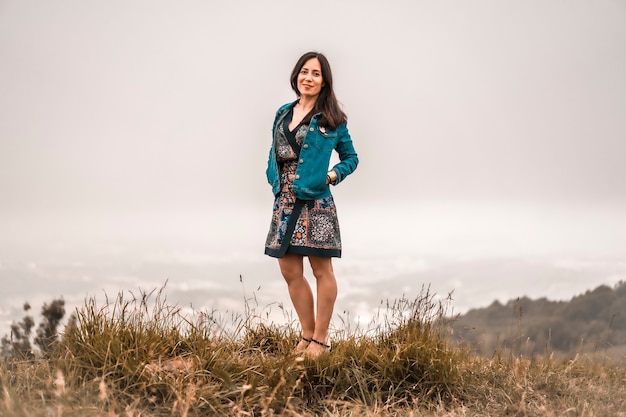 Mode de vie, fille brune profitant de la nature avec une robe colorée et une veste au sommet d'une montagne