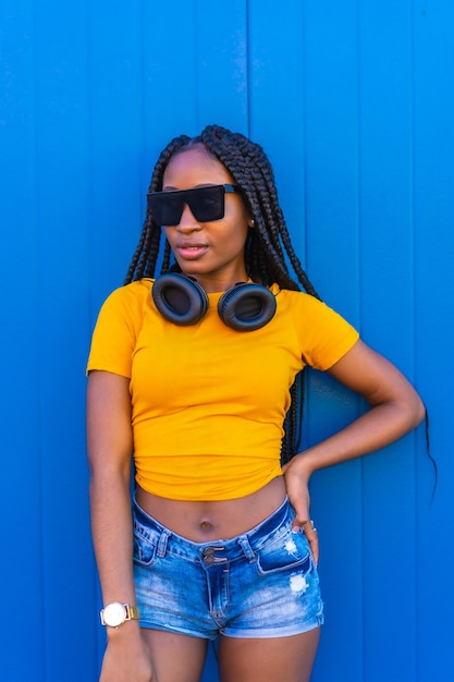 Mode de vie, fille noire aux longues tresses, dans une chemise jaune et des lunettes de soleil. Dj avec un casque souriant