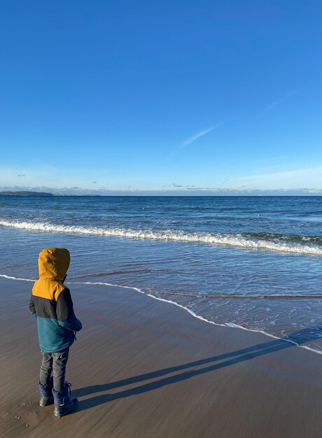 Mode de vie heureux Un petit garçon se promène par une journée froide et ensoleillée le long du bord de mer