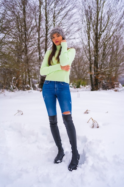 Mode de vie d'hiver, portrait caucasien brunette avec tenue verte et bonnet de laine profitant de la neige à côté de pins enneigés, vacances dans la nature