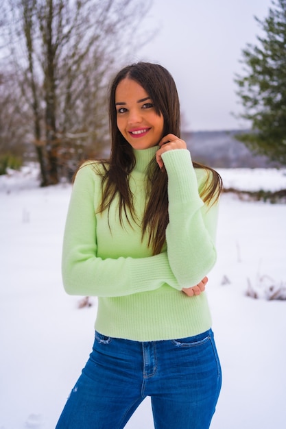 Mode de vie d'hiver, portrait jeune femme caucasienne brune avec tenue verte et jeans, souriant dans la neige, vacances dans la nature