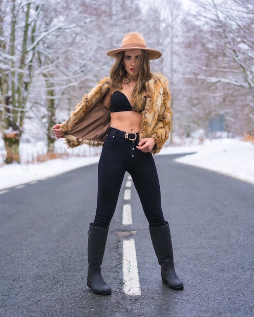 Mode de vie hivernal, modèle marchant en sous-vêtements, un chapeau de cowboy et un pull léopard sur la route dans la forêt gelée