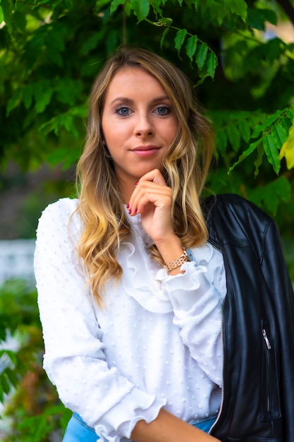 Mode de vie, une jeune femme d'affaires blonde de race blanche dans un parc de la ville, portant une veste en cuir et un T-shirt blanc