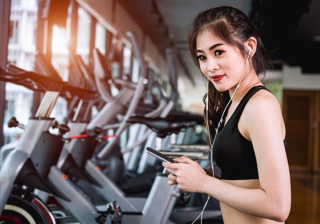 Mode de vie de jeune femme à l'aide de smartphone jouer de la musique sur tapis roulant en cours d'exécution à la salle de fitness