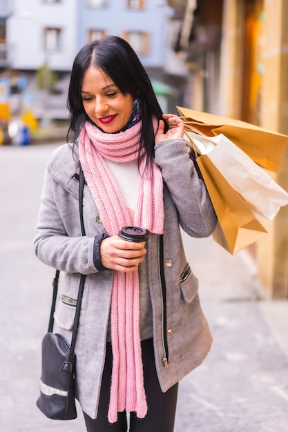 Mode de vie d'une jeune fille brune de race blanche, faire du shopping dans la ville avec des sacs en papier et un café à emporter