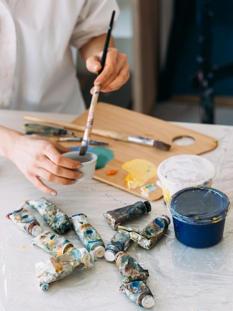Mode de vie de peintre Fournitures d'art Lieu de travail créatif Mains d'artistes professionnelles mélangeant de la peinture avec un pinceau à table avec une palette de tubes et des outils