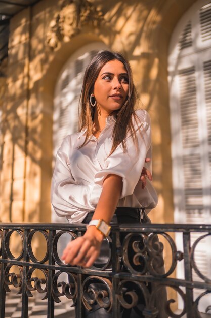 Mode de vie, regard doux d'une jeune brune dans une jupe en cuir noire et une chemise blanche sur une balustrade noire d'une maison traditionnelle un après-midi d'automne