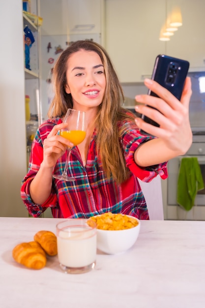 Photo mode de vie sain, blonde caucasienne avec un jus d'orange pour le petit déjeuner et enregistrement d'une vidéo pour les réseaux sociaux