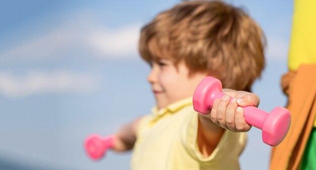 Mode de vie sain. Enfant de remise en forme. Enfant exerçant avec des haltères. Sport pour les petits enfants. Garçon sportif avec des haltères. Sport. Forme, santé et énergie. Un garçon joyeux fait des exercices avec des haltères