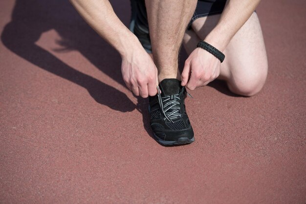 Mode de vie sain et entraînement, coureur, lacets de chaussures à nouer sur une piste de course ensoleillée en plein air en vêtements de sport. activité et sport d'été