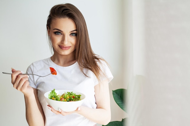 Mode de vie sain femme mangeant de la salade souriante heureuse dans une cuisine légère