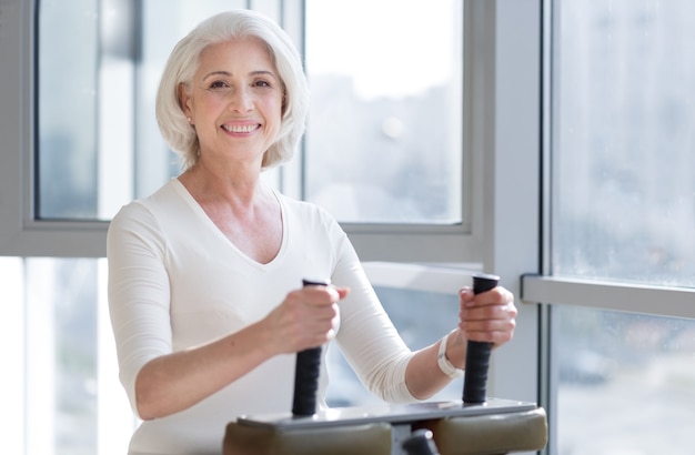 Mode de vie sain. Femme senior sportive ravie souriant et exerçant tout en faisant une session dans la salle de gym.