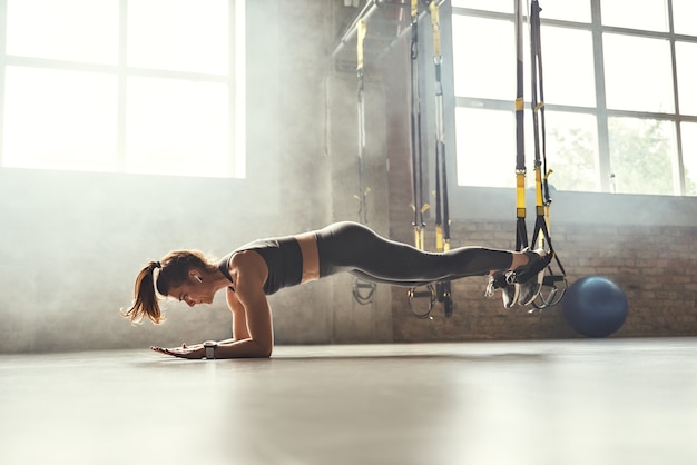 Mode de vie sain jeune femme athlétique faisant une planche avec des sangles de fitness trx dans la salle de sport