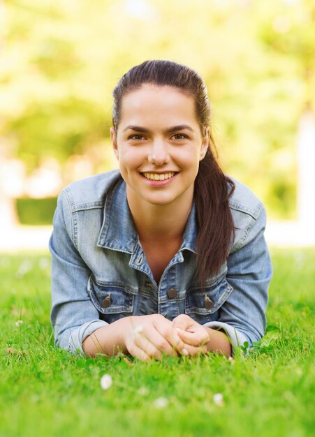 mode de vie, vacances d'été, loisirs et concept de personnes - jeune fille souriante allongée sur l'herbe dans le parc