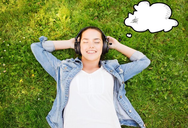 mode de vie, vacances d'été, technologie, musique et concept de personnes - jeune fille souriante dans un casque allongé les yeux fermés sur l'herbe