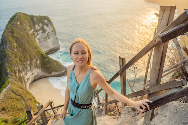 Mode de vie de vacances en famille Une femme heureuse se tient au point de vue Regardez la belle plage sous une haute falaise Destination de voyage à Bali Endroit populaire à visiter sur l'île de Nusa Penida