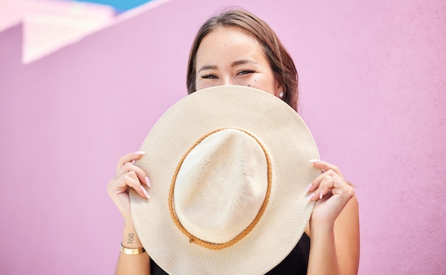 Mode de voyage et chapeau d'été avec une femme touriste dans la ville sur un fond de mur rose pastel Joyeuses vacances et touriste avec une voyageuse couvrant son visage avec un chapeau de soleil en ville