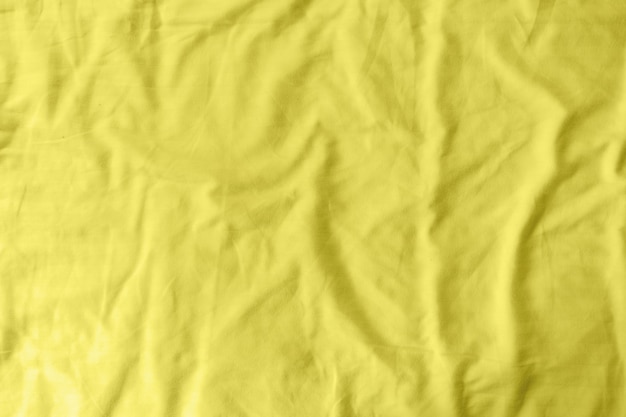 Modèle abstrait d'un drap de lit froissé jaune dans une chambre d'hôtel. La fabrication du drap de lit utilise du coton, du lin, du modal de soie et de la rayonne de bambou. Couleur tendance de l'année 2021 - jaune éclairant