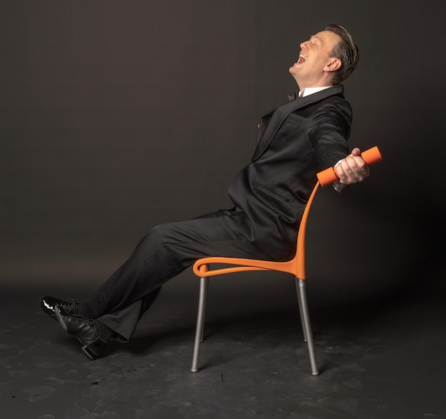 Modèle d'affaires homme macho élégant haltères assis chaise gentleman smoking noeud papillon costume homme d'affaires