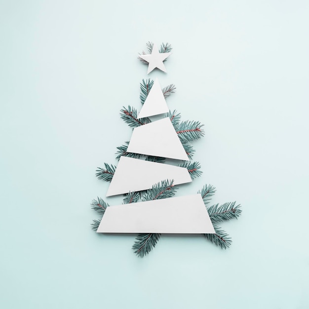 Modèle d'arbre de Noël minimaliste créatif avec des branches d'arbres de Noël bleus et des formes géométriques blanches sur un fond bleu pastel