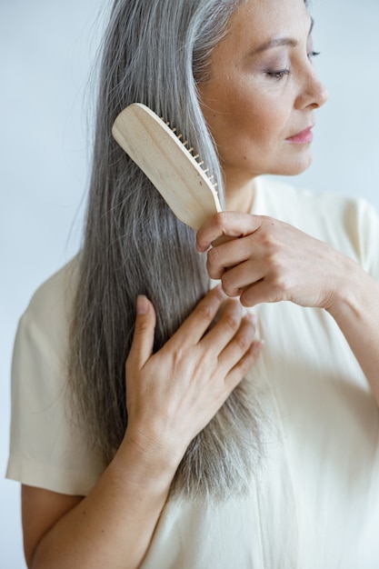 Modèle asiatique d'âge moyen tranquille brosse de longs cheveux blancs posant sur fond clair