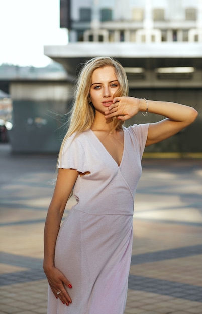 Modèle assez blonde vêtue d'une robe rose tendance profitant d'une chaude soirée d'été. Concept de mode de rue