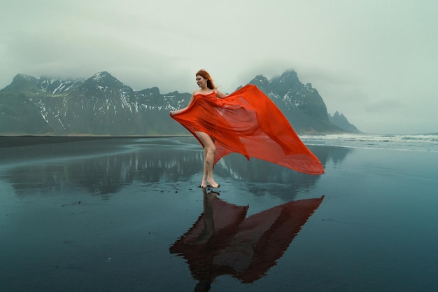 Modèle attrayant en robe rouge sur la photographie panoramique de la plage de Reynisfjara