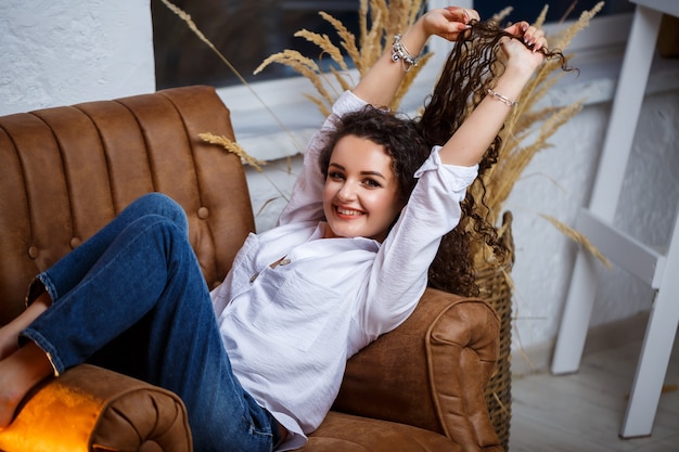 Modèle de belle jeune fille avec des boucles posant. Elle porte une chemise blanche et un jean.