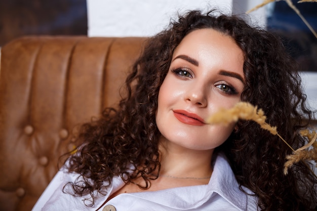 Modèle de belle jeune fille avec des boucles posant. Elle porte une chemise blanche et un jean.