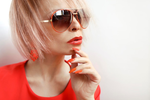 Modèle blonde avec maquillage des lèvres orange et lunettes de soleil