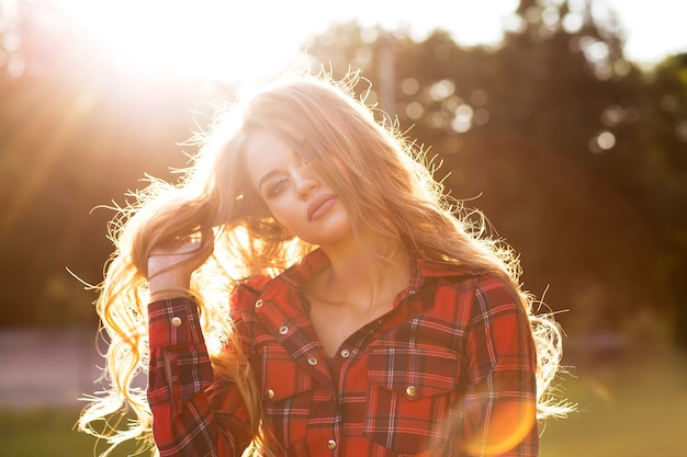 Modèle blonde à la mode en robe à carreaux posant dans les rayons du soleil