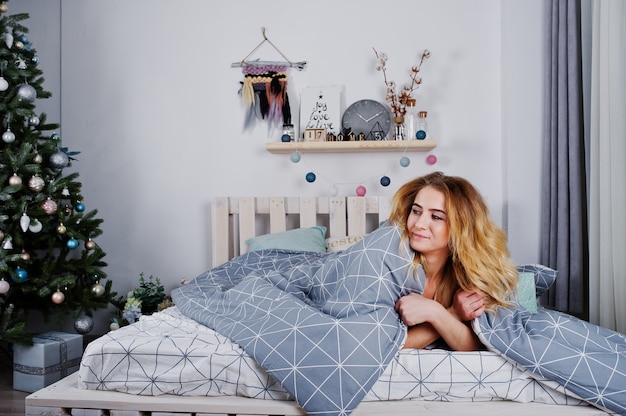 Modèle blonde nue sexy sur le lit avec des coffrets cadeaux de Noël contre l'arbre du nouvel an.