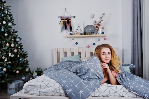 Modèle blonde nue sexy sur le lit avec des coffrets cadeaux de Noël contre l'arbre du nouvel an.