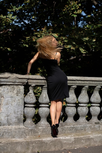 Modèle blonde séduisante aux cheveux longs vêtue d'une robe noire, posant près des balustres