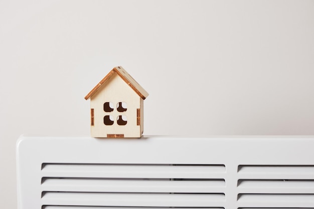 Modèle en bois d'une maison sur un radiateur électrique pour chauffer la maison, espace de copie, utilisant le radiateur dans le concept de saison froide