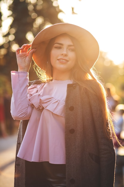 Modèle brune heureuse portant un chapeau, un chemisier et un manteau posant dans le parc en automne